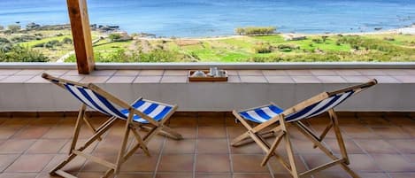 Una terraza con dos sillas de playa a rayas que dan a vistas del océano y un paisaje verde.