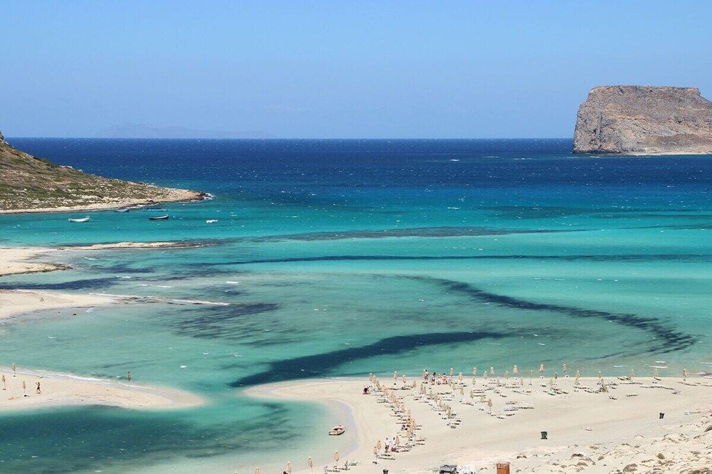 Une plage côtière aux eaux turquoise et limpides, bordée d’un rivage sablonneux et agrémentée d’une formation rocheuse imposante.