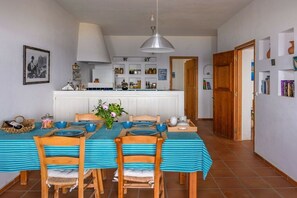A dining area with a long table, chairs, and a kitchen in the background. - Villa in Sfinari with swimming pool (Sfinari)
