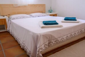 A neatly made bed with a white bedspread and two folded towels, a wooden headboard, and a nightstand with a bottle and glasses. - Villa in Sfinari with swimming pool (Sfinari)