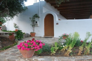 A white building with a wooden door and steps leading up to it. There are potted plants and flowers in front of the building. - Villa in Sfinari with swimming pool (Sfinari)