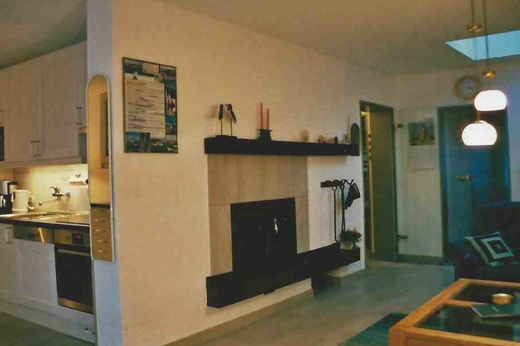Eine moderne Küche mit weißen Schränken, einem eingebauten Backofen und einer schwarzen Arbeitsplatte. Ein Kamin mit Sims und ein an der Wand befestigter Kleiderhaken sind ebenfalls vorhanden.