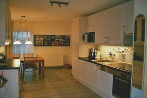 A compact kitchen with white cabinets, a microwave, a sink, and a dining area with chairs and a table. - Holiday home with 2 bedrooms (Wangerland)