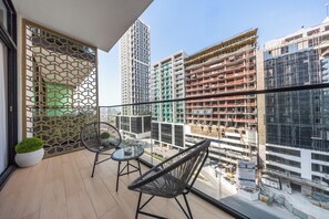A balcony with two chairs and a small table, overlooking a cityscape with modern buildings and construction sites. - StayShort - Peace and Tranquility in this 1 Bedroom in JVC (Dubai)
