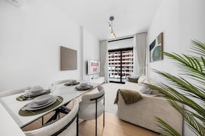 A modern living room with a dining area, a sofa, and a view of a building under construction. - StayShort - Peace and Tranquility in this 1 Bedroom in JVC (Dubai)