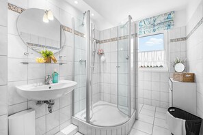 A modern bathroom with a glass-enclosed shower, a sink with a mirror above, and a window with a view of the sky. - Dünenblick – Arrive. Breathe. See the Sea. Feel the Holiday. (Schönberg (Holstein))