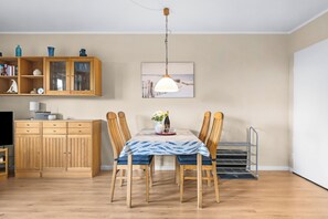 Ein Essbereich mit einem Tisch für vier Personen, Holzkästen, einer hängenden Leuchte und einem Schrank mit Glastüren.