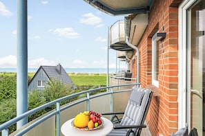 A balcony with a table set for a meal, overlooking a grassy area and a body of water. - Dünenblick – Arrive. Breathe. See the Sea. Feel the Holiday. (Schönberg (Holstein))