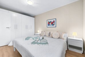 A bedroom with a large bed, white wardrobe, bedside tables with lamps, and a framed artwork on the wall. - Dünenblick – Arrive. Breathe. See the Sea. Feel the Holiday. (Schönberg (Holstein))