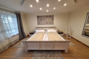 Ein Doppelbett mit Holzrahmen, zwei Nachttische, ein an der Wand befestigtes Kunstwerk und ein Fenster mit Vorhängen.