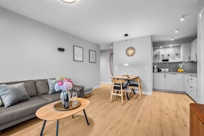 A modern living room with a sofa, a dining table with chairs, a kitchen area with cabinets, and a wall clock. - Haus Elisabeth, Apartment 1, on the beach, with underground parking, Wi-Fi, and a balcony (Sylt)