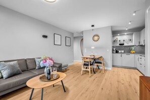 Ein modernes Wohnzimmer mit Sofa, Esstisch mit Stühlen, Küchenzeile mit Schränken und einer Wanduhr.