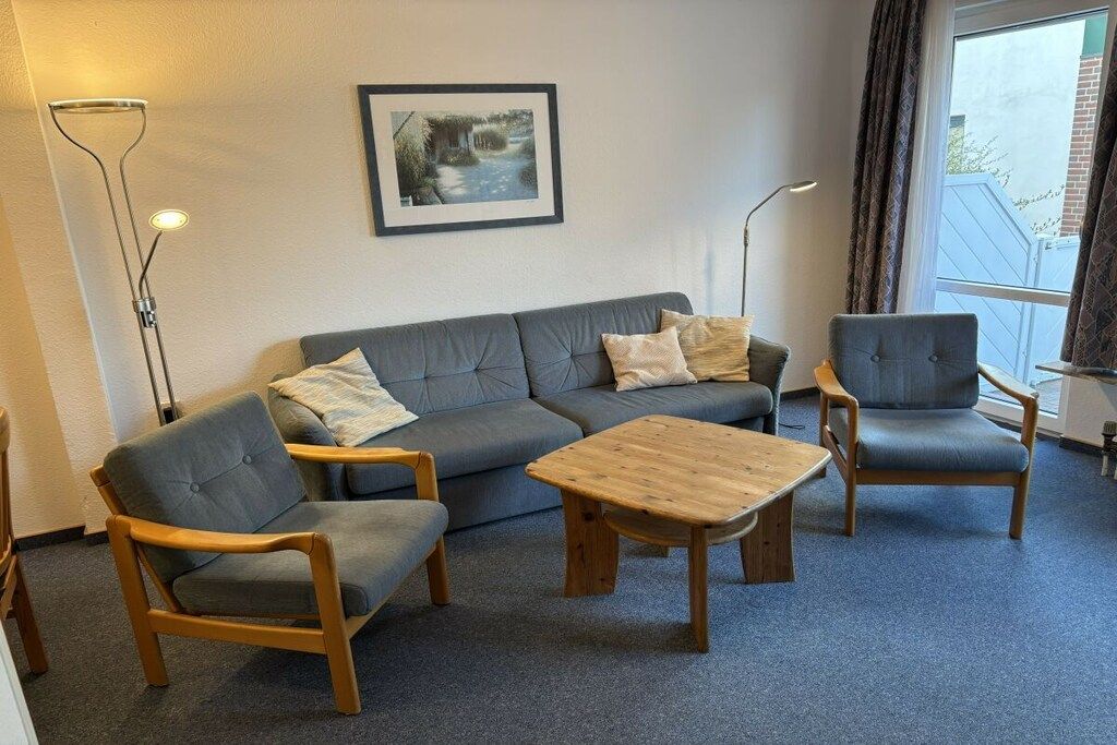 Una habitación con un sofá gris, dos sillones, una mesa de centro de madera y una lámpara de pie.