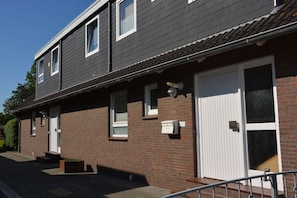 A two-story residential building with a brick facade, a white garage door, and a small porch area. - Apartment 1 - Seestein Holiday Home (Borkum)