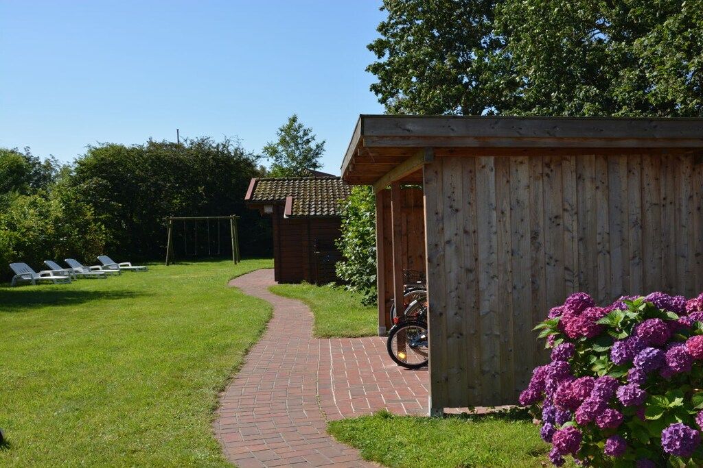 Une structure en bois, accessible par un chemin pavé de briques, entourée de verdure et sous un ciel dégagé.