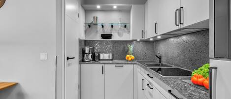 Una cucina moderna con mobili bianchi, un piano di lavoro in granito, un lavello in acciaio inossidabile e un forno integrato.
