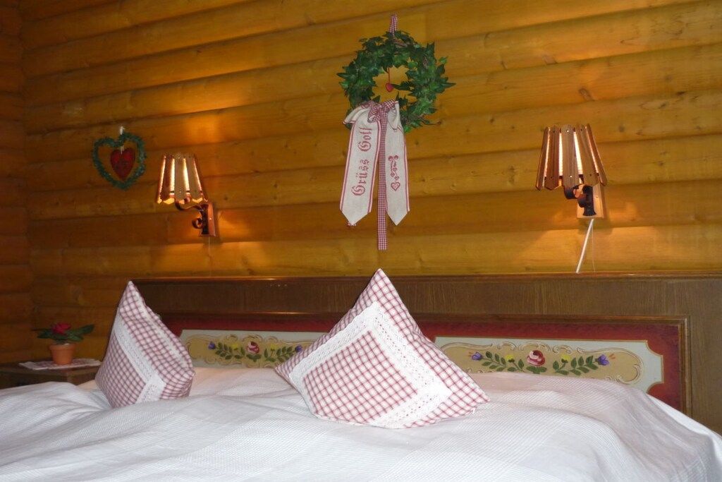 Habitación de hotel con techo de madera, cama con ropa blanca, almohadas decorativas, lámparas de pared y una corona en la pared.