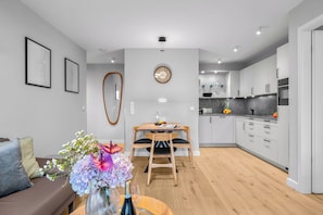 A modern kitchen with white cabinets, a dining area with a wooden table and chairs, and a living room with a brown sofa and a vase of flowers. - Haus Elisabeth, Apartment 2, on the beach, with an underground parking space, Wi-Fi, and a balcony (Sylt)