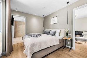 Ein modernes Schlafzimmer mit einem großen Bett, Nachttischen, einem Flachbildfernseher und einer kleinen Sitzecke mit Sofa und Tisch.