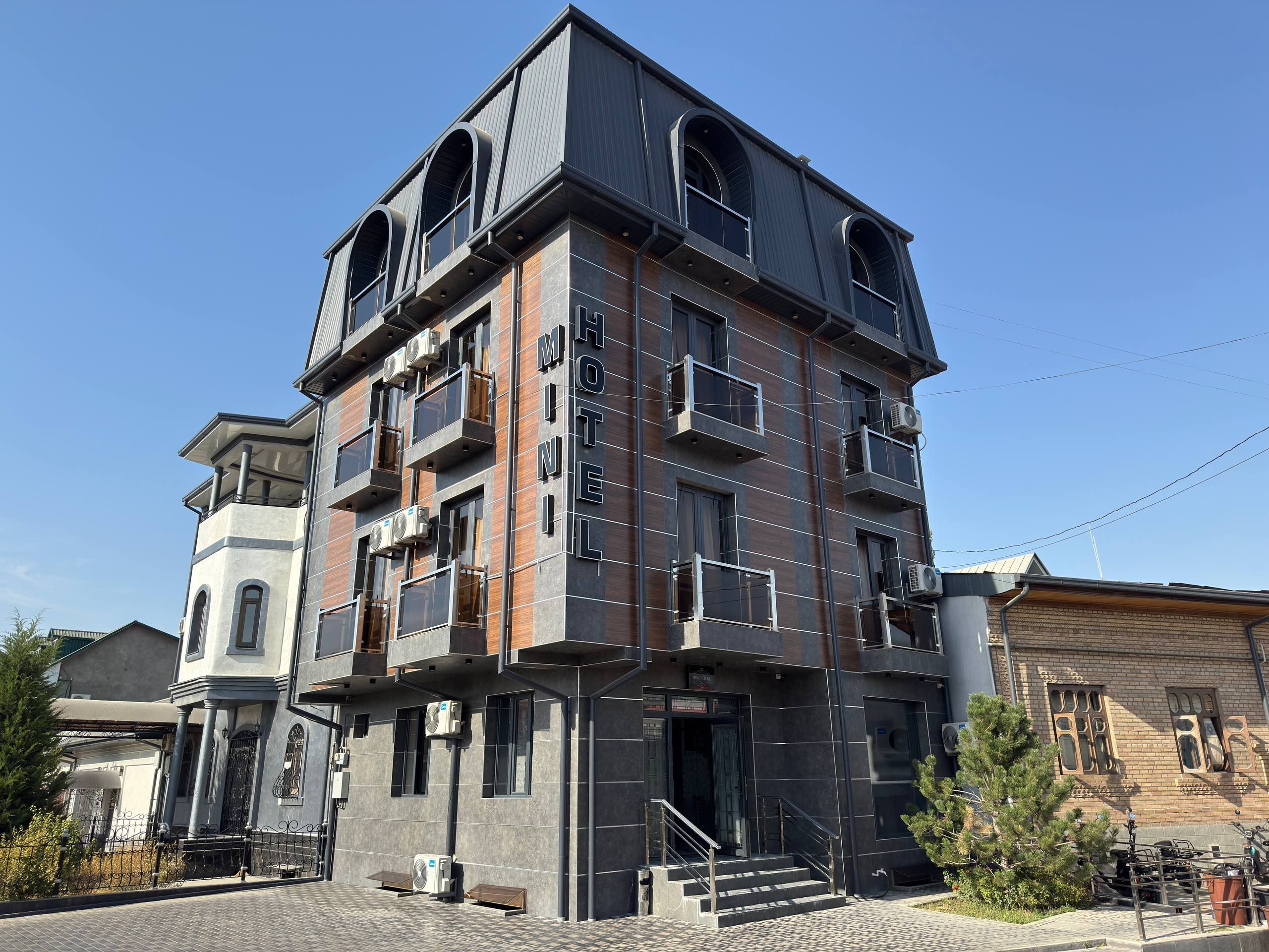 Un hotel de varios pisos con balcones, una escalera y una zona de entrada pavimentada.