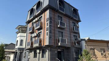Un hotel de varios pisos con balcones, una escalera y una zona de entrada pavimentada.