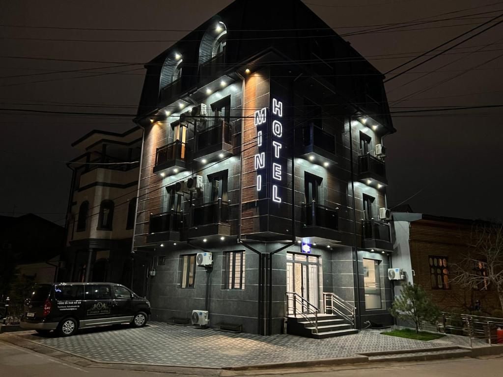 Un hotel de varios pisos con un llamativo letrero que dice 'HOTEL', una escalera que conduce a la entrada y un vehículo estacionado al frente.