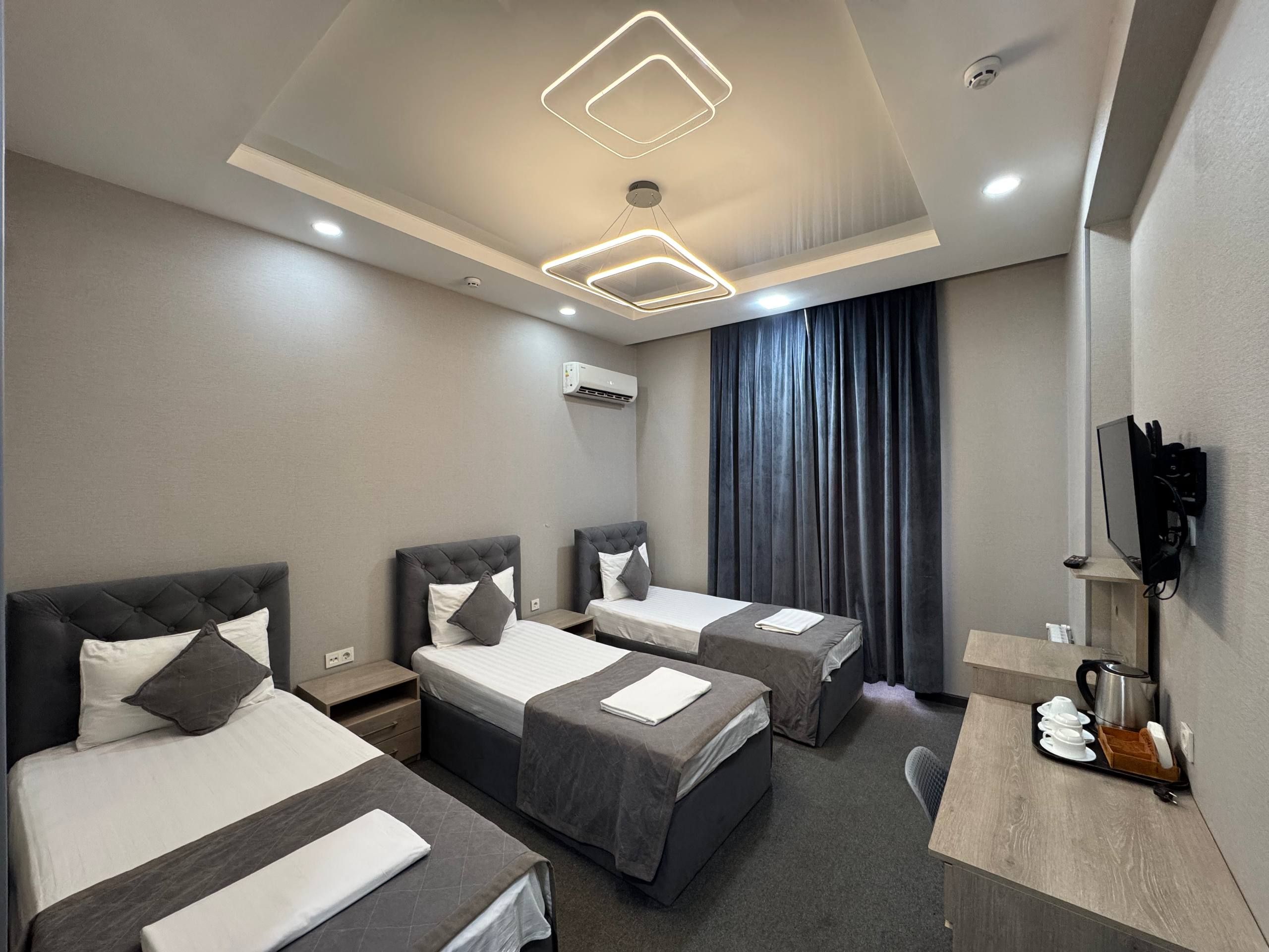 Habitación de hotel con dos camas, un escritorio con cafetera y un televisor montado en la pared.