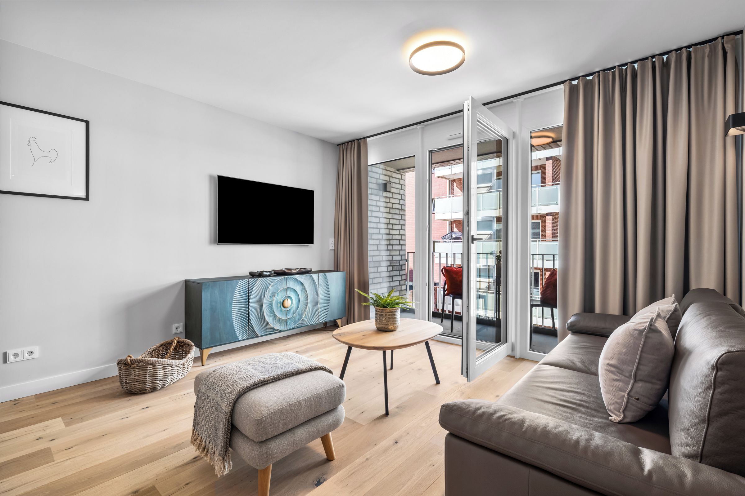 Ein modernes Wohnzimmer mit Flachbildfernseher, einer Couch, einem Couchtisch und Blick auf einen Balkon mit Stadtansicht.