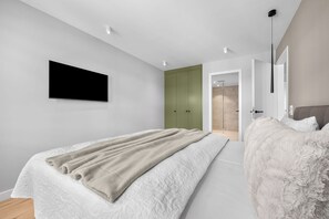 A modern bedroom with a bed, a television mounted on the wall, and a walk-in closet. - Haus Elisabeth, Apartment 6, on the beach, with an underground parking space, Wi-Fi, and a balcony (Sylt)