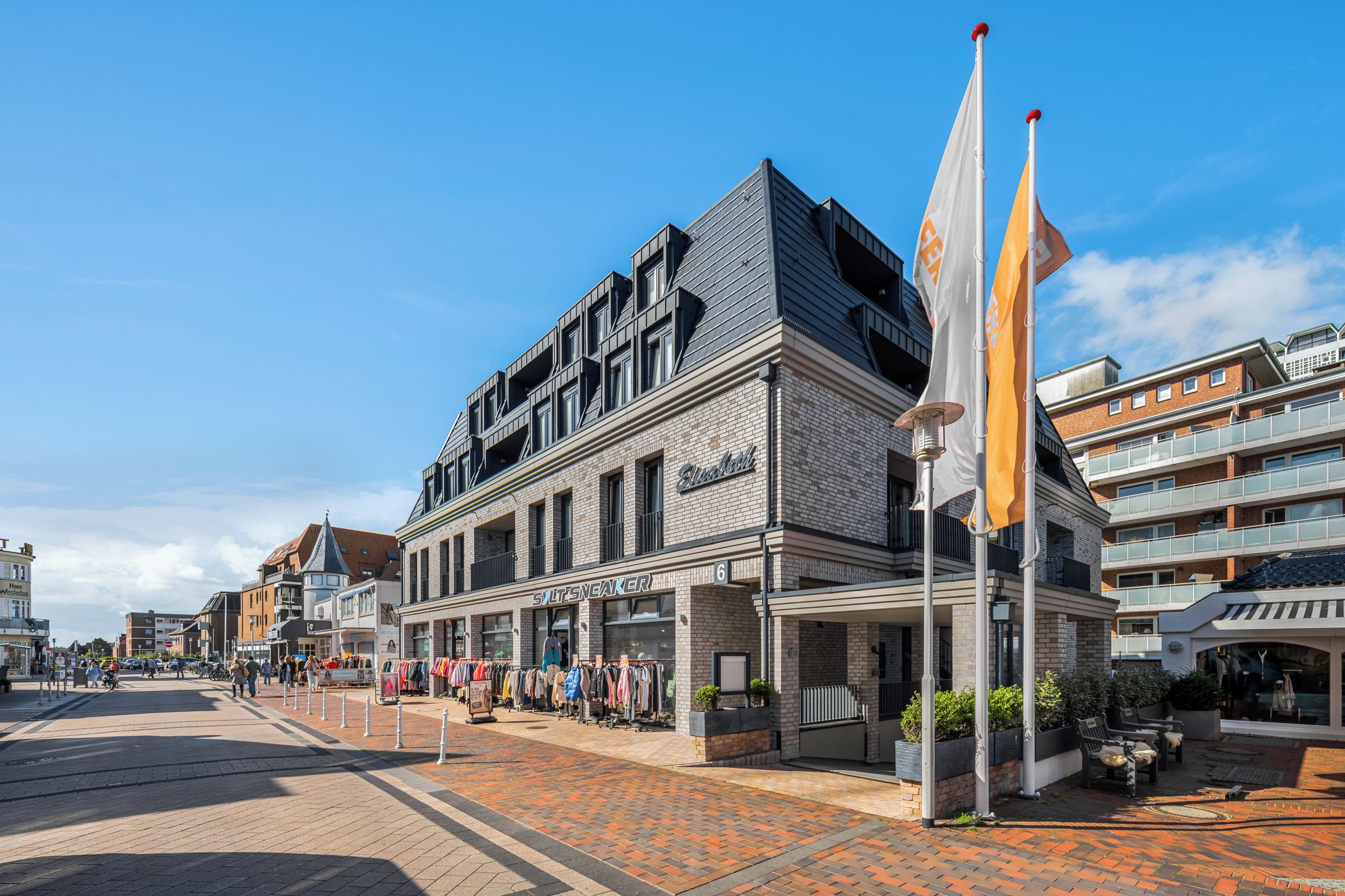 Un bâtiment moderne avec une façade en briques, une devanture de magasin avec une enseigne et un mât sur lequel flotte un drapeau.