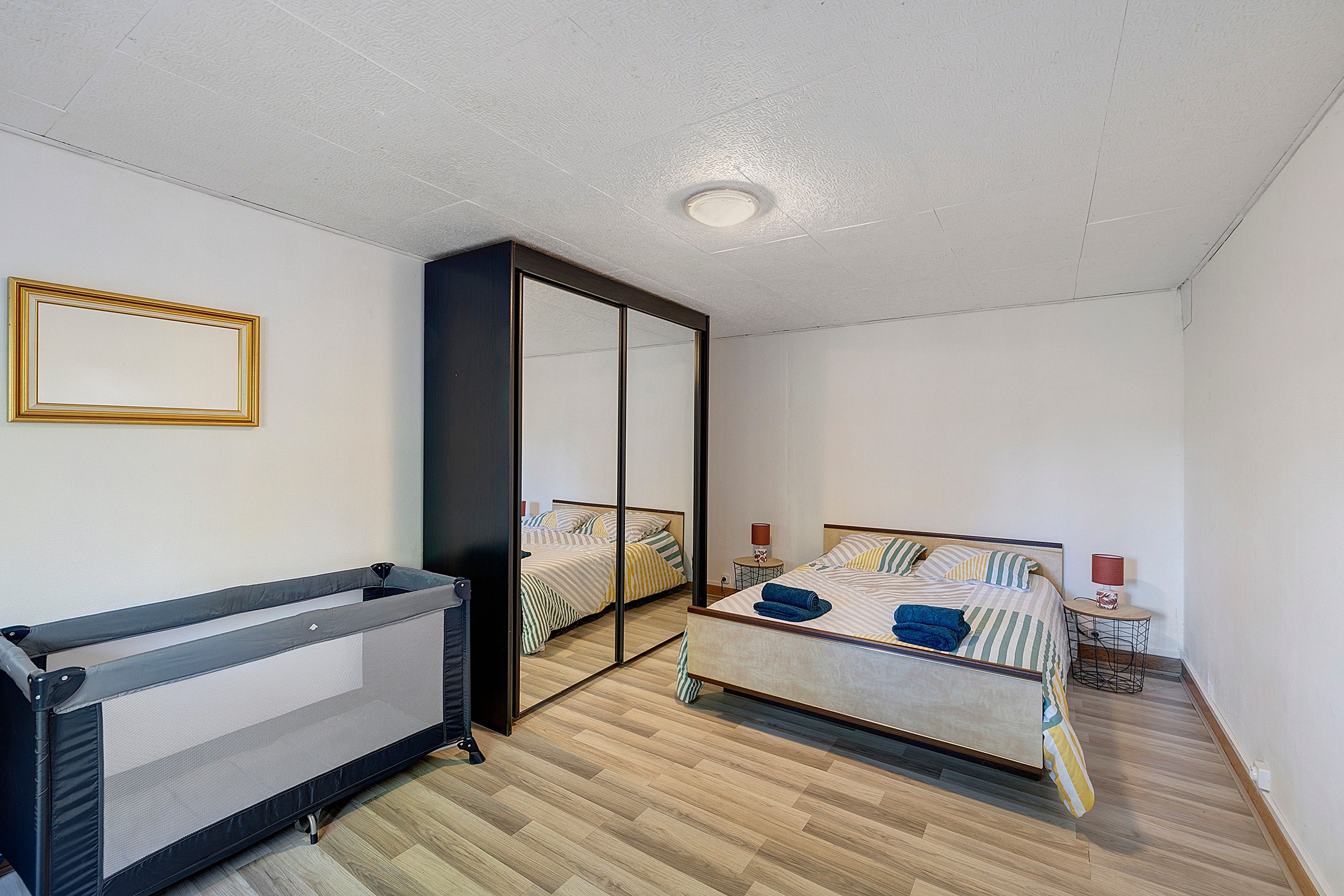 Une chambre à coucher avec un lit, un miroir, un radiateur et une petite table avec une lampe.