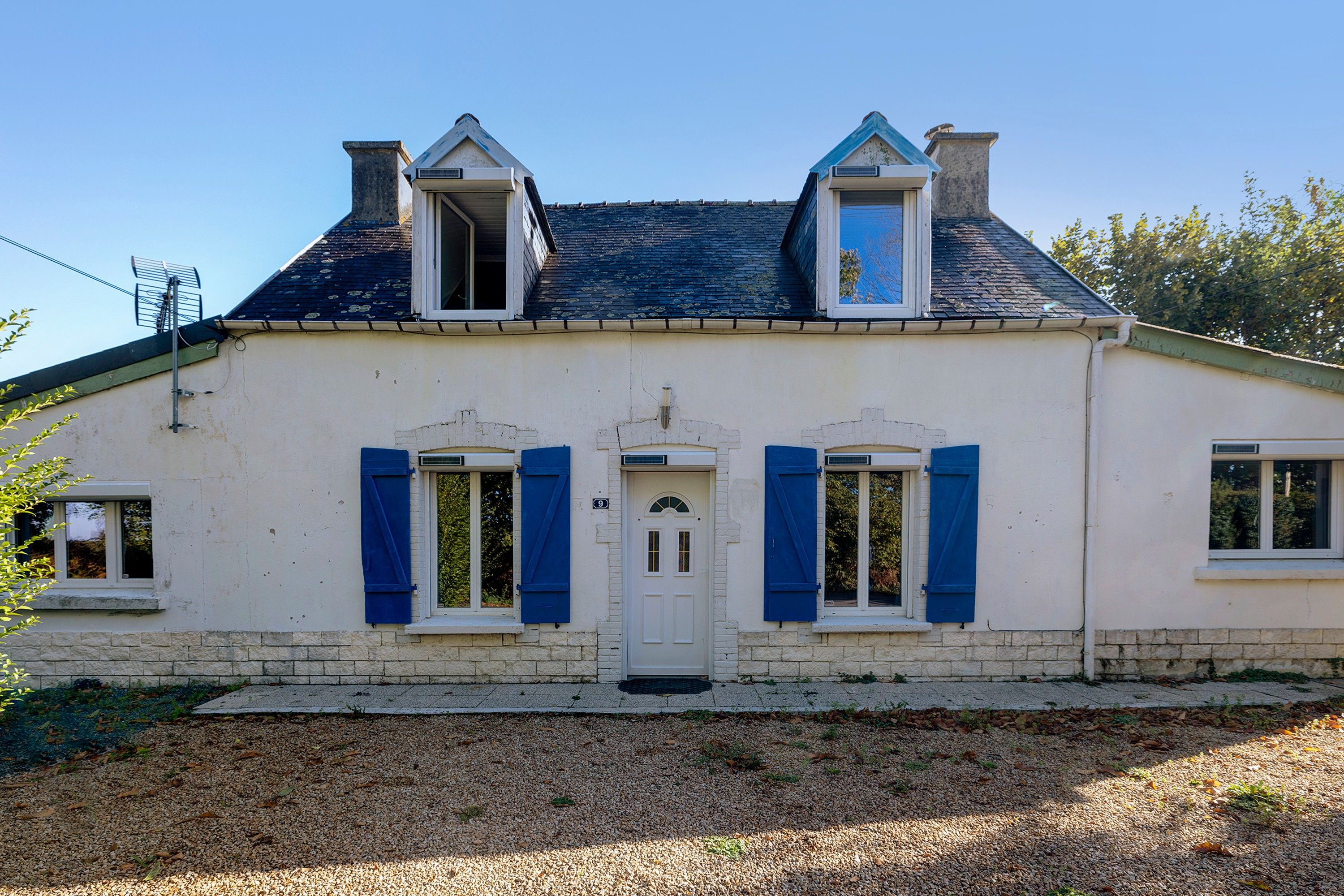Una casa de dos pisos con fachada blanca, contraventanas azules y tejado gris.