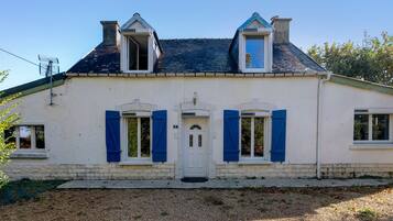 Una casa de dos pisos con fachada blanca, contraventanas azules y tejado gris.