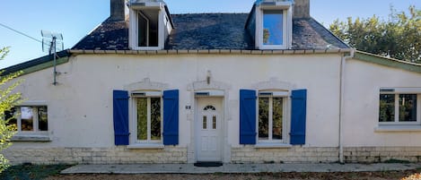 A two-story house with a white facade, blue shutters, and a grey roof.