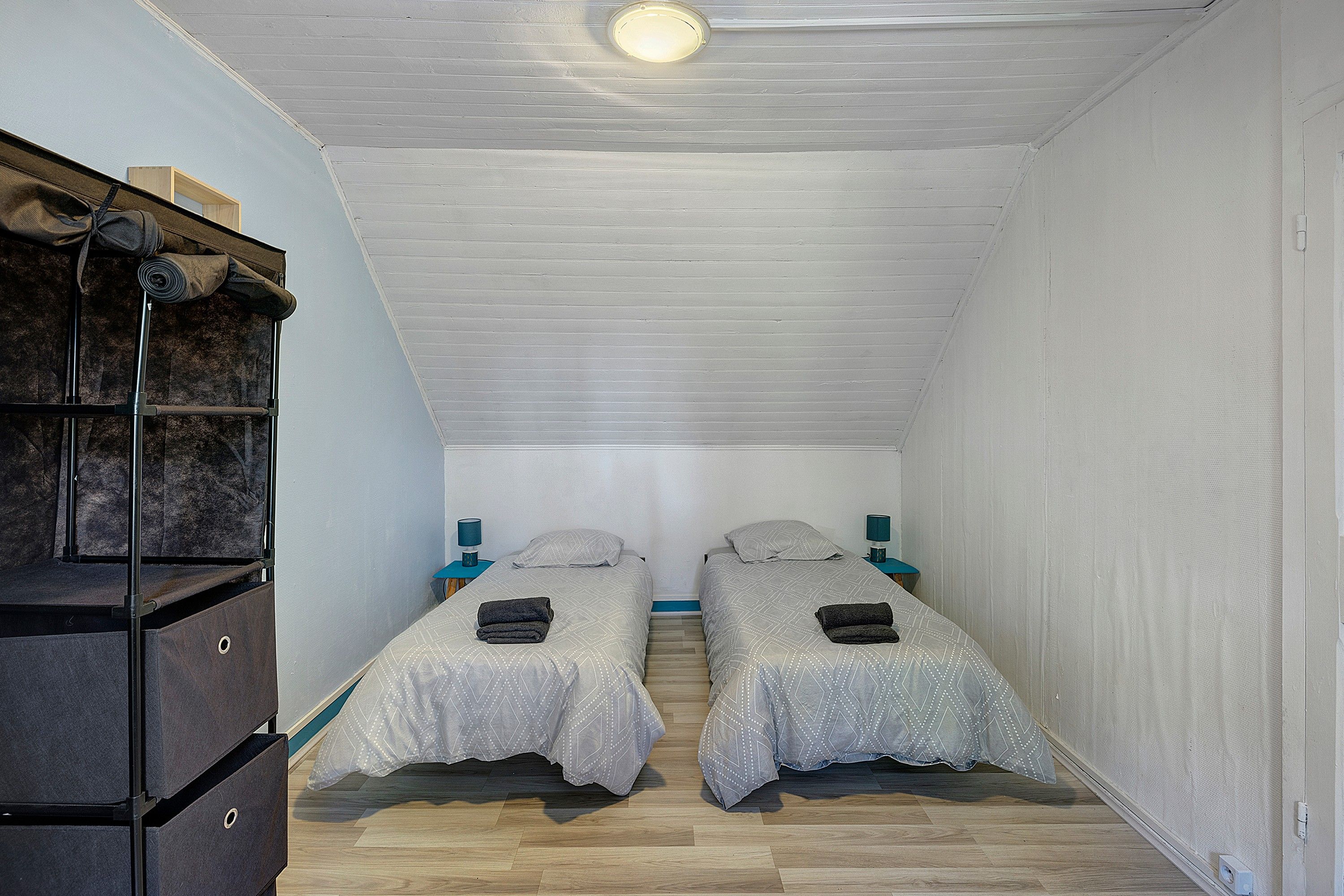 Ein kleines, kompaktes Zimmer mit zwei Einzelbetten, Holzboden und einer integrierten Regallösung an einer Seite.