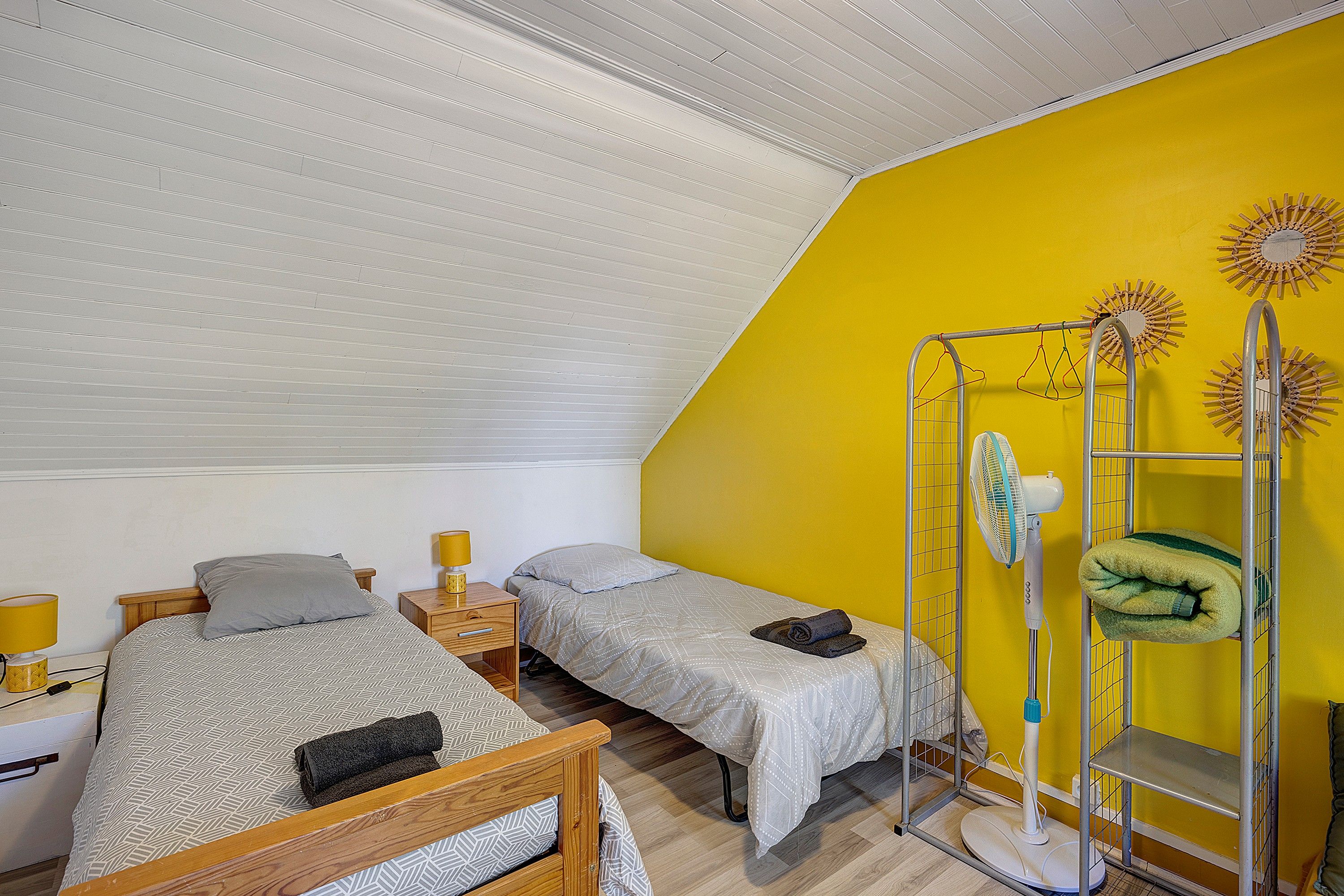 Une chambre avec deux lits, un ventilateur de plafond et un mur d’accent jaune.