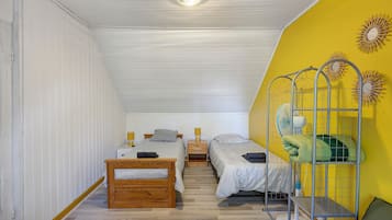 Una habitación con dos camas, piso de madera, pared amarilla y una lámpara en el techo.