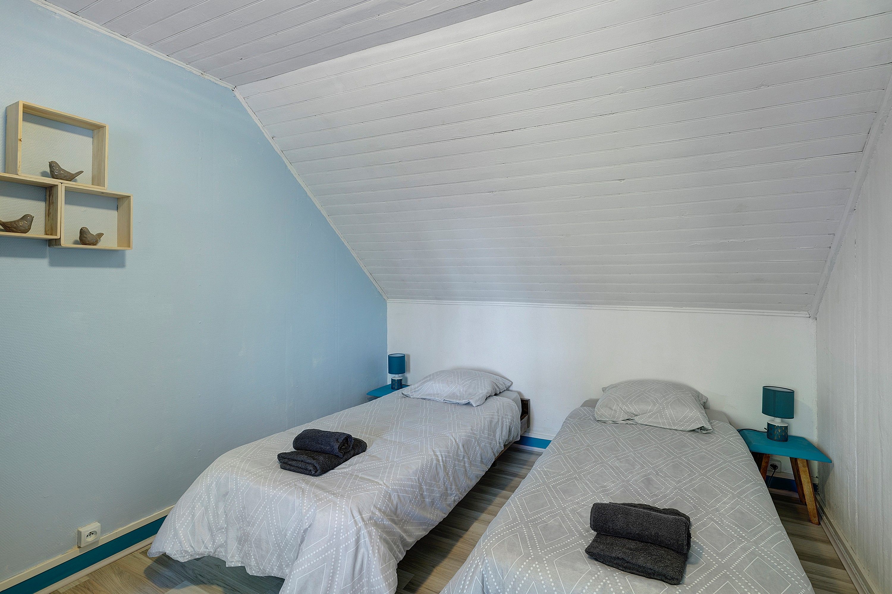 Un alojamiento pequeño, de una sola habitación, con dos camas, techo inclinado y pared de color azul claro.