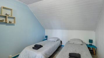 Un alojamiento pequeño, de una sola habitación, con dos camas, techo inclinado y pared de color azul claro.