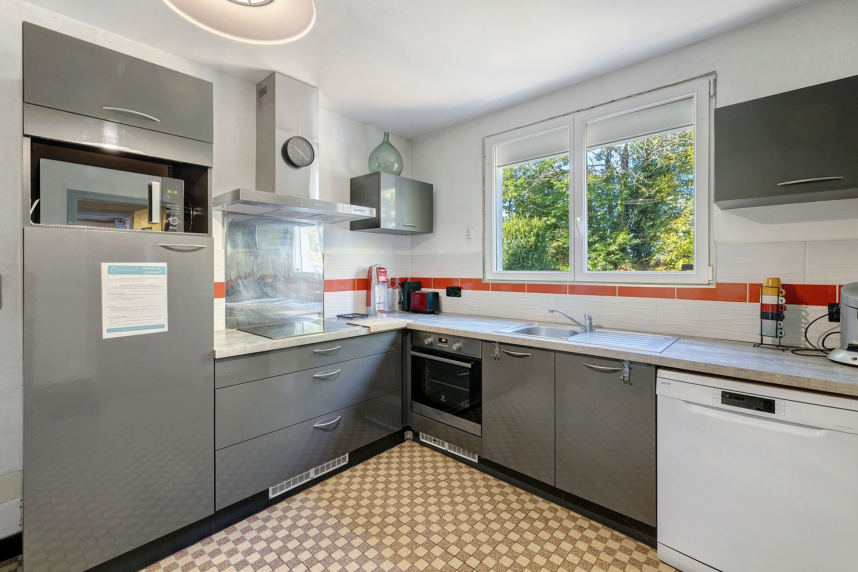 A compact kitchen with a built-in oven, a dishwasher, and a window providing a view of greenery outside.