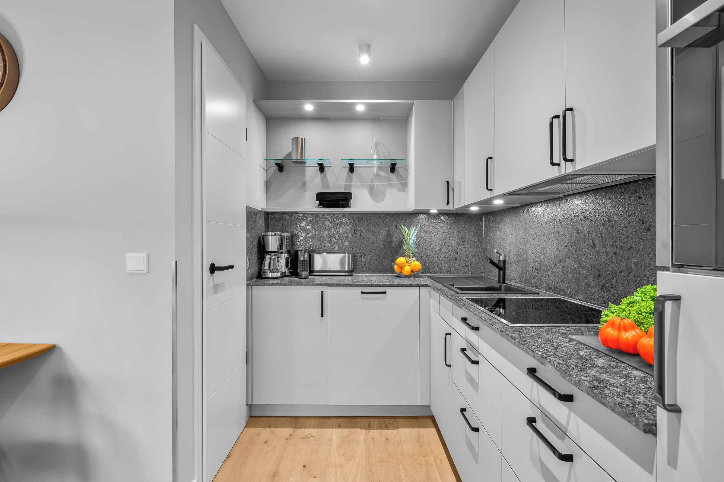 A modern kitchen with white cabinets, a granite countertop, a stainless steel sink, and a built-in oven.