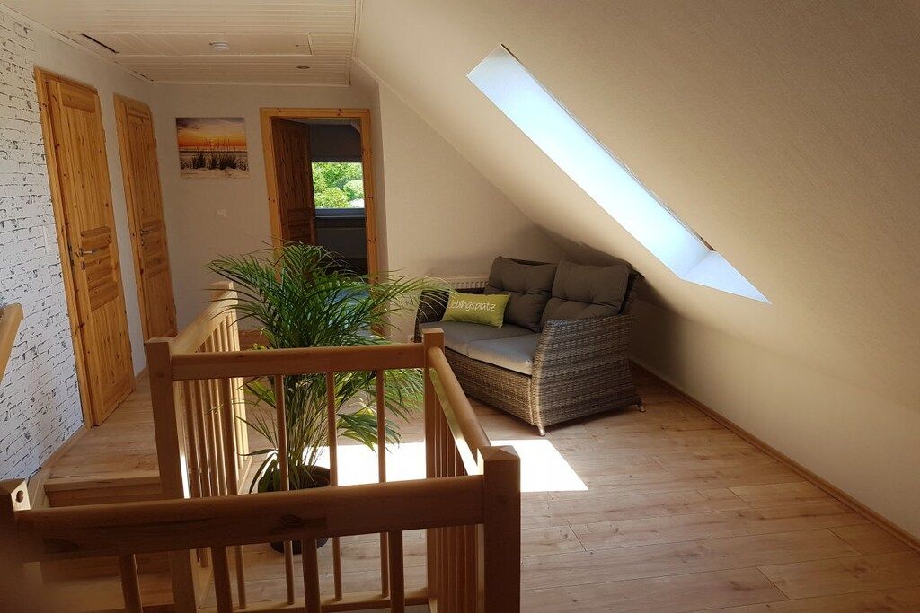 A loft bedroom with a sloped ceiling, wooden flooring, a sofa, and a potted plant.