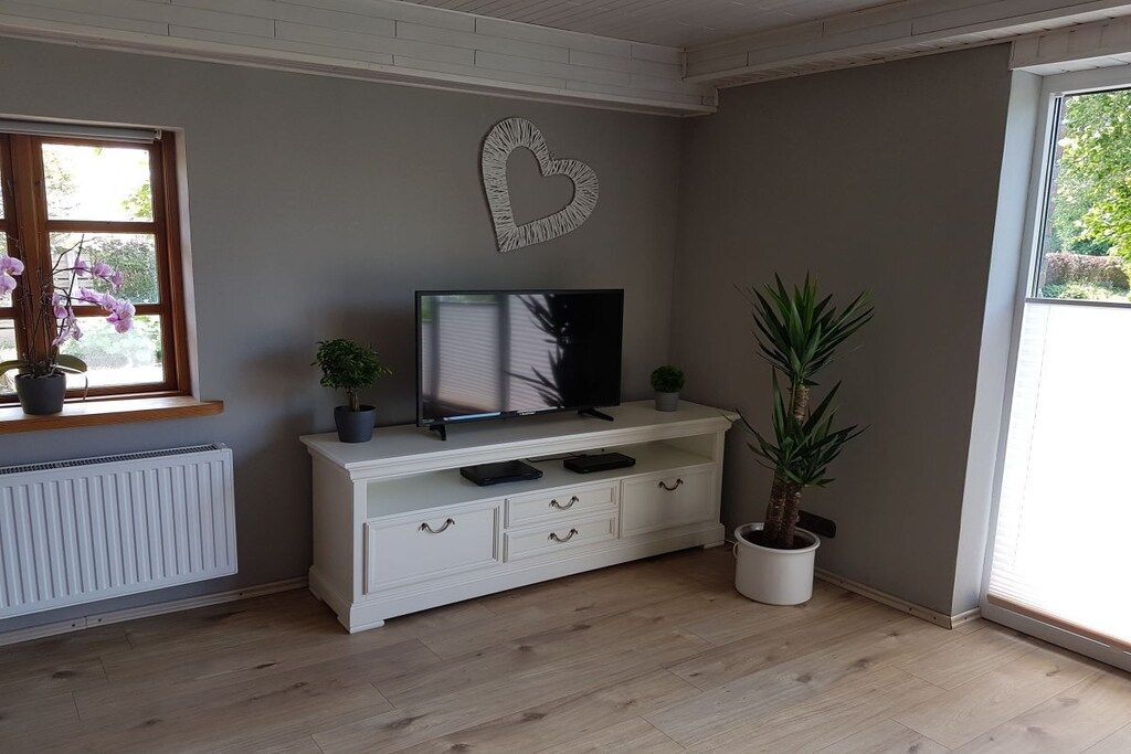 A room with a white cabinet, a flat-screen TV, a heart-shaped wall decoration, and a potted plant.