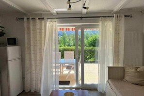 A room with a bed, a table, and a view of a garden through a sliding door. - Holiday apartment with 1 bedroom (Arrach)