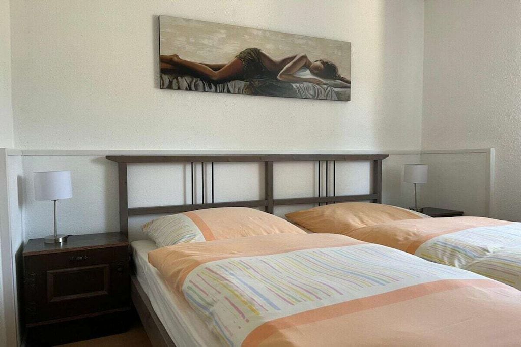 Una habitación de hotel con cama, mesitas de noche, lámparas y un cuadro en la pared.