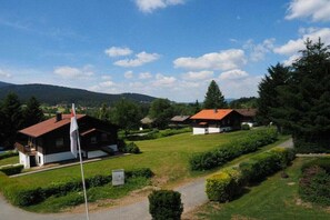 Ländliche Szenerie mit einem Haus mit rotem Dach, umgeben von grünen Feldern und Bäumen.