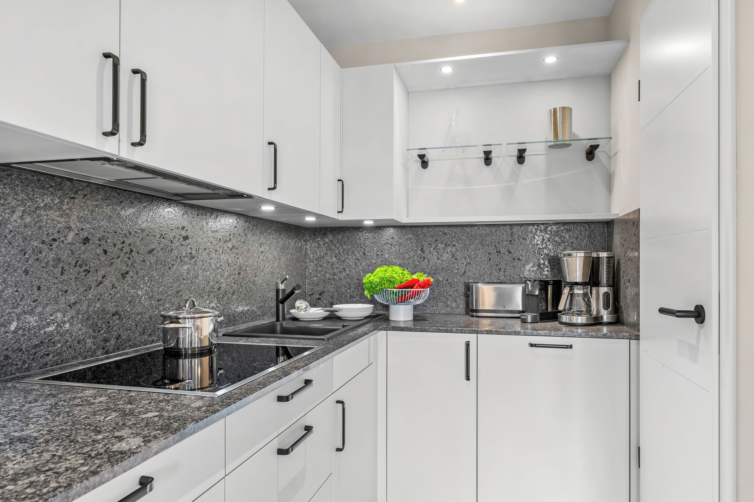 A modern kitchen with white cabinets, a granite countertop, a stainless steel stove, and a coffee maker.