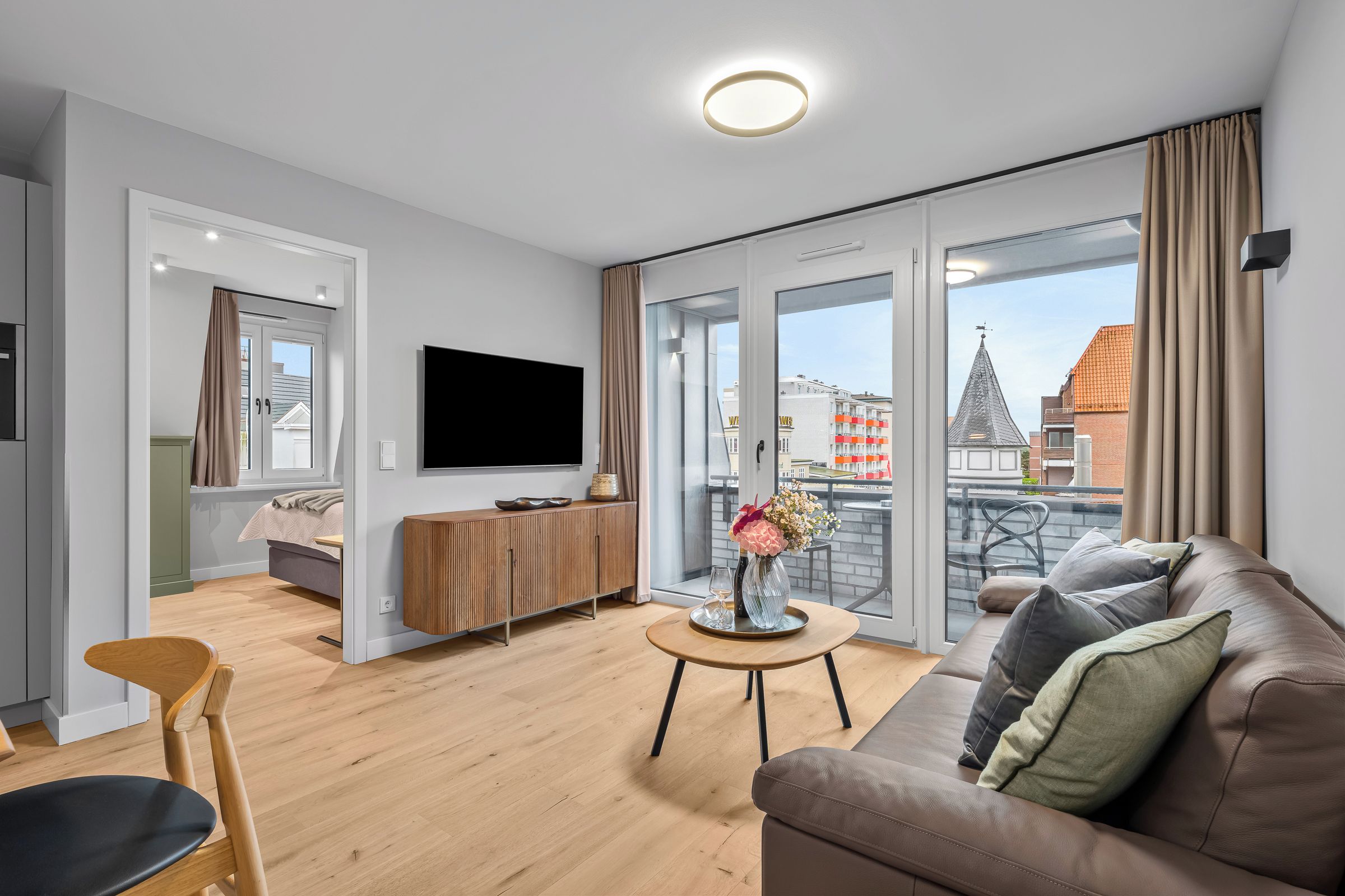 Una sala de estar moderna con un sofá, un televisor, un mueble de madera y un balcón con vista a edificios.