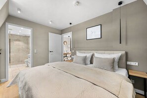 Ein modernes Schlafzimmer mit einem großen Bett, einem Nachttisch, einer Wandleuchte und einem gerahmten Bild.
