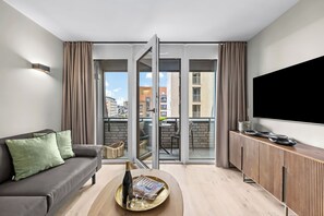 Uma sala de estar moderna com sofá, mesa de centro com garrafa e copos, televisão e varanda com vista para edifícios.
